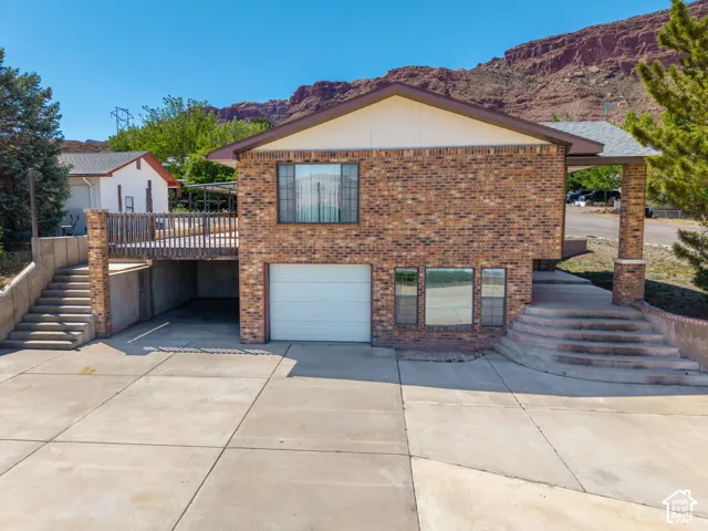 Brick exterior residence featuring a front-facing garage, elevated wood deck, and concrete driveway