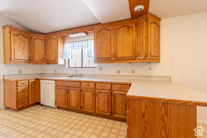 Kitchen featuring extensive wood cabinetry, L-shaped white laminate countertops, and a built-in white dishwasher
