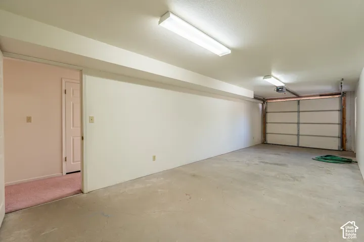 Spacious garage with concrete flooring, fluorescent lighting, a roll-up garage door, and direct interior access