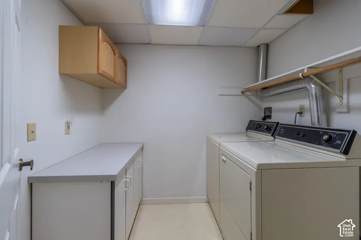 Dedicated laundry area featuring a drop ceiling, upper wood-finish cabinetry, a white countertop, and base cabinetry with white doors