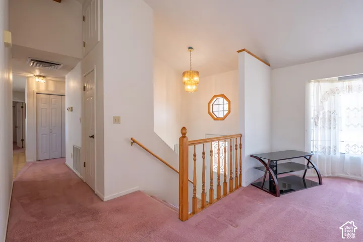 Carpeted interior area featuring a wooden staircase with baluster railing, a decorative octagonal window, and a chandelier-style light fixture