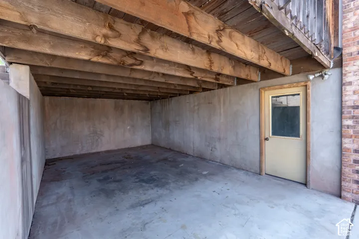 Under-deck concrete patio offering a protected outdoor space with exposed wood joists and a privacy door