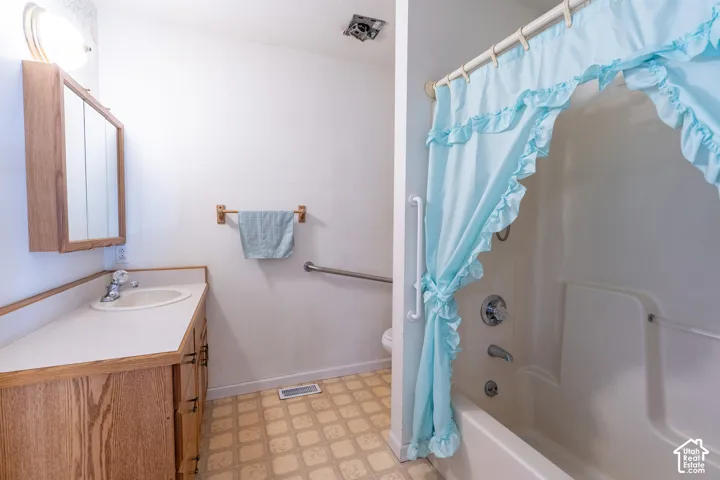 Bathroom featuring a wood-finish vanity with a laminate countertop, built-in medicine cabinet, and patterned vinyl flooring