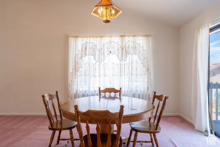 Dining area featuring vaulted ceilings, a central chandelier, and a large window with privacy curtains