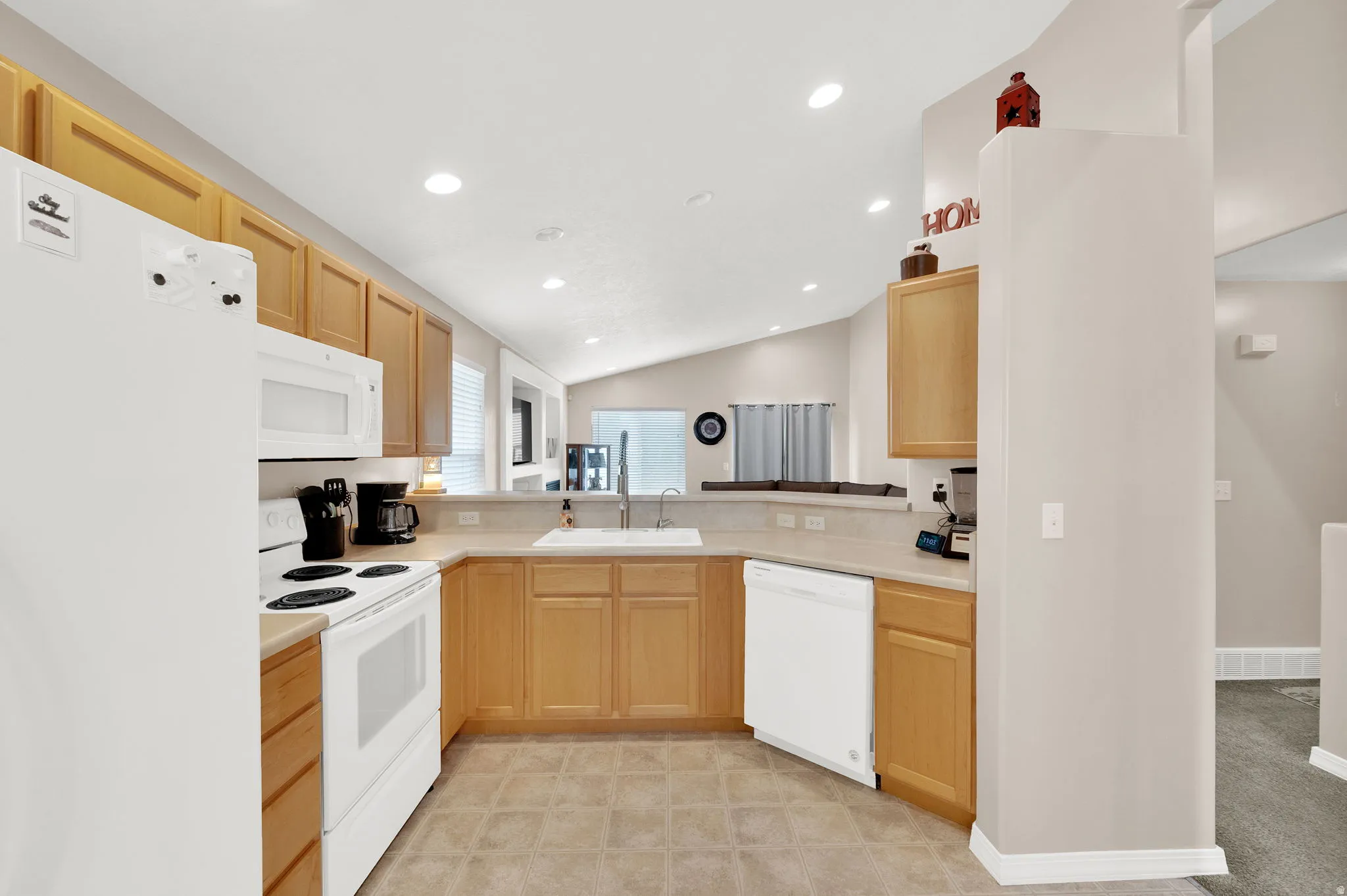 Kitchen featuring light wood-finish cabinetry, white appliances, and a double basin sink