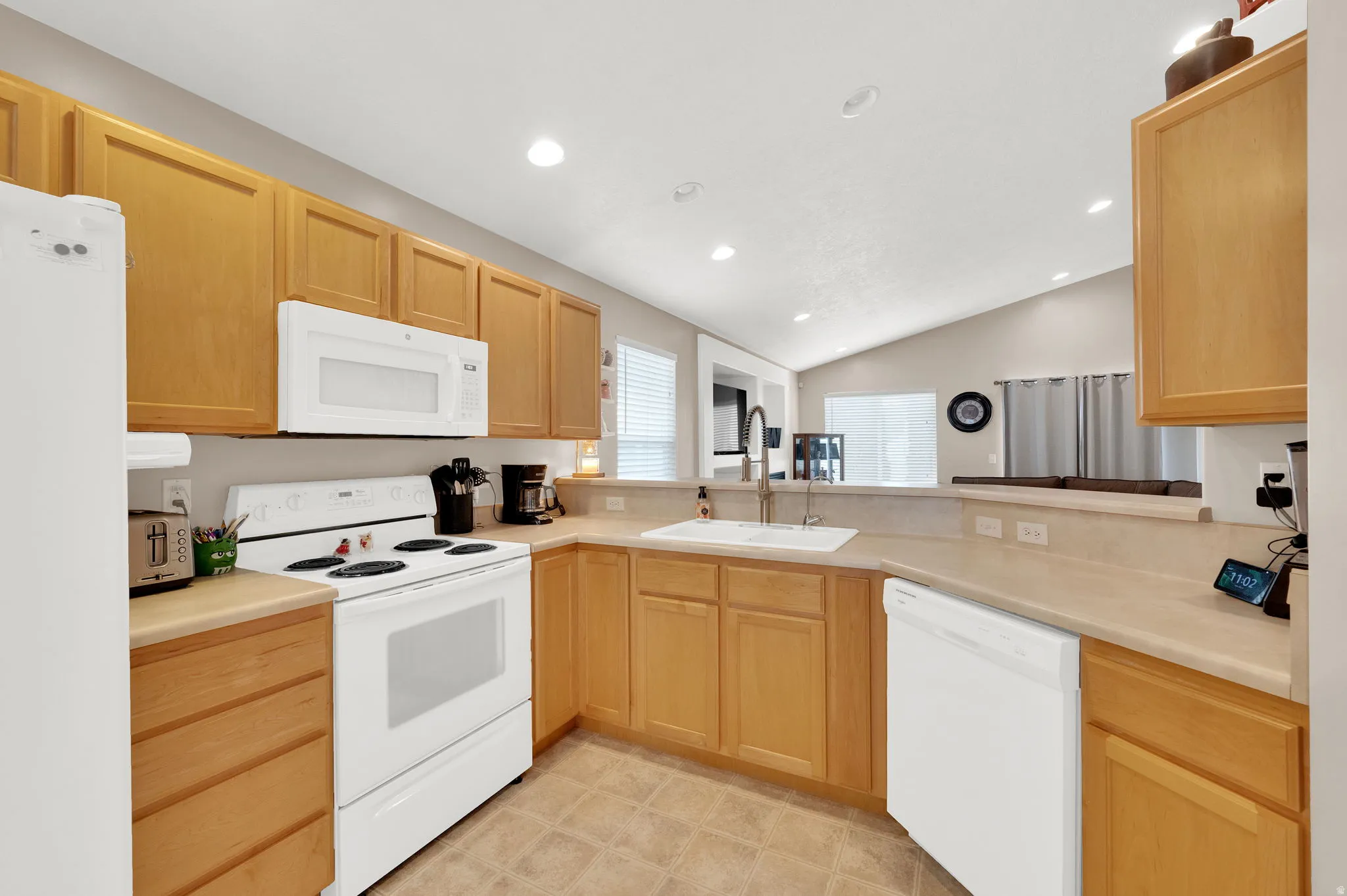 Kitchen featuring light wood cabinetry, white appliances, a white sink with a gooseneck faucet, light countertops, and recessed lighting