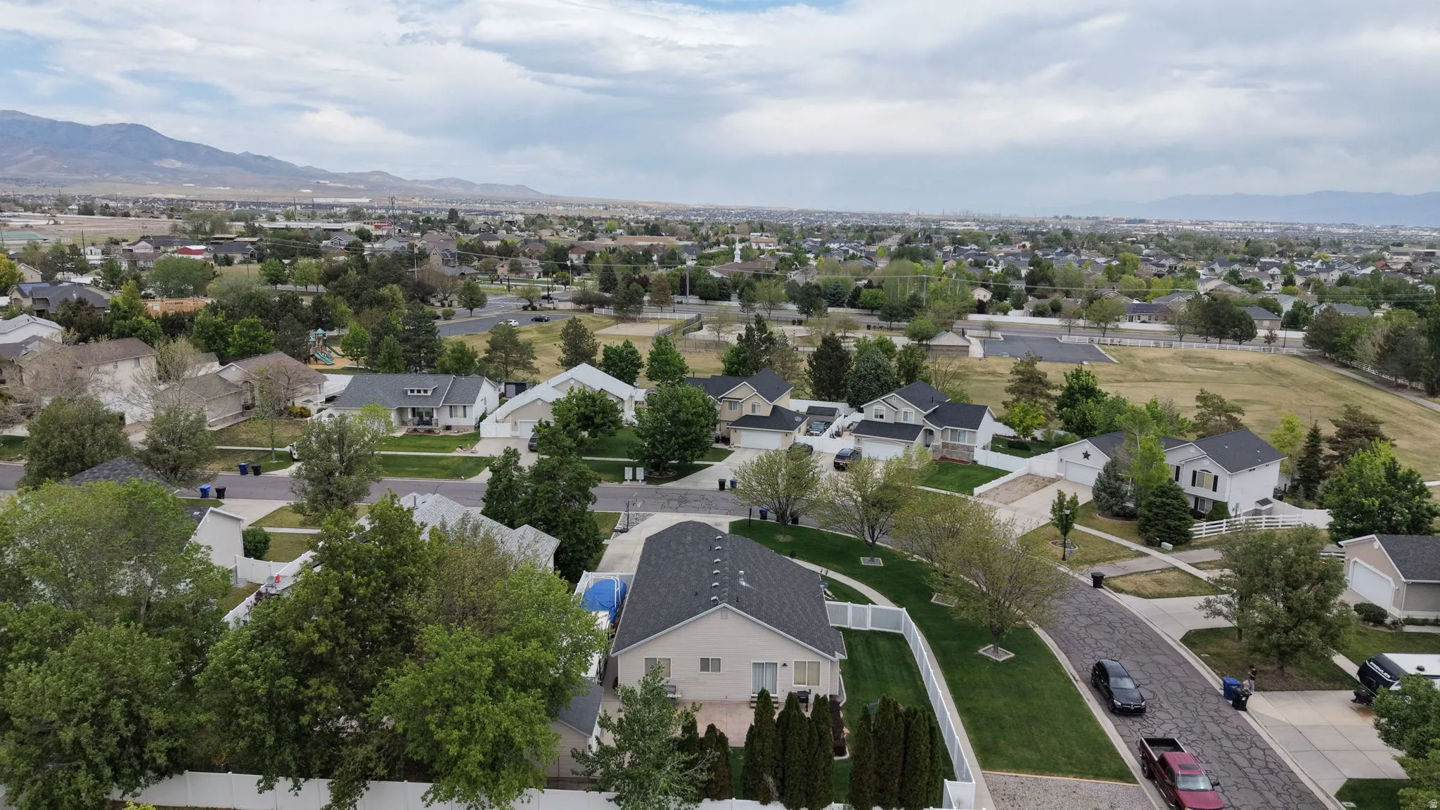Aerial perspective of a residential neighborhood featuring diverse single-family homes with pitched roofs, mature trees, and manicured lawns
