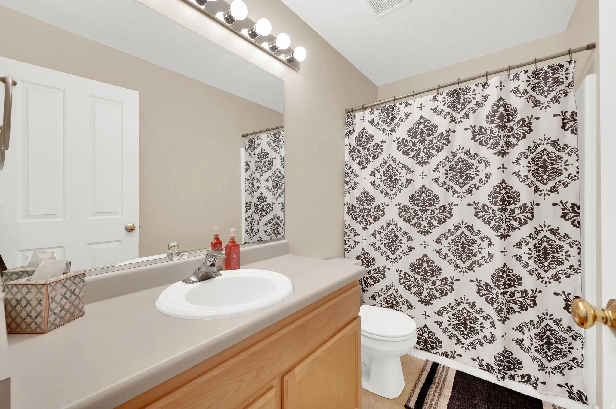 Bathroom featuring a light wood-finish vanity with an integrated white sink, a spacious countertop, and a large wall-mounted mirror