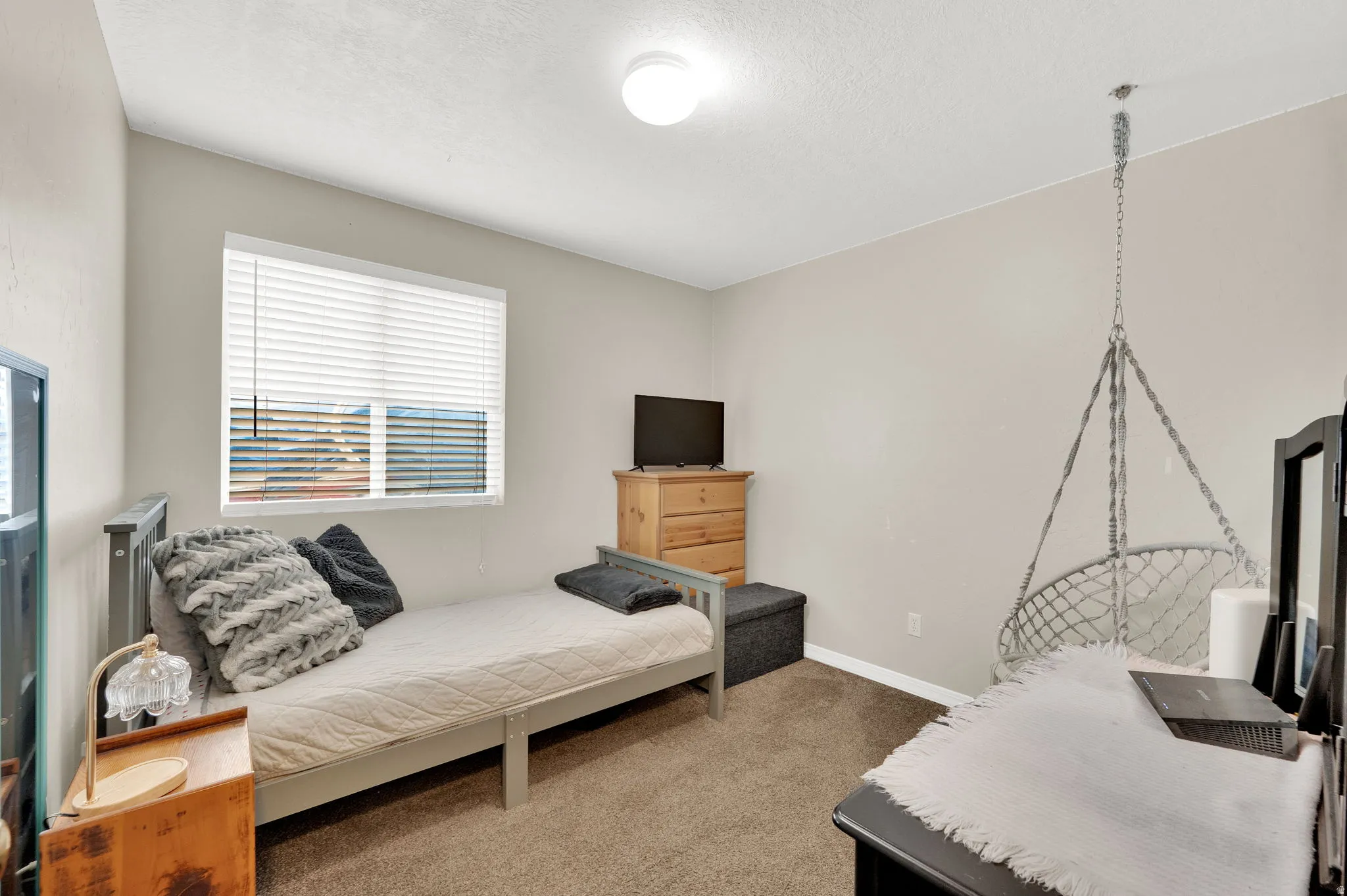 Neutral-toned walls and carpeted flooring define this room, featuring a single window with horizontal blinds