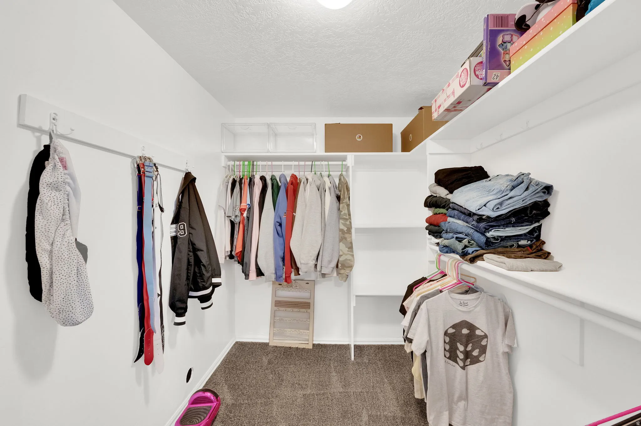 Walk-in closet featuring white built-in shelving, white hanging rods, and neutral-toned carpeting