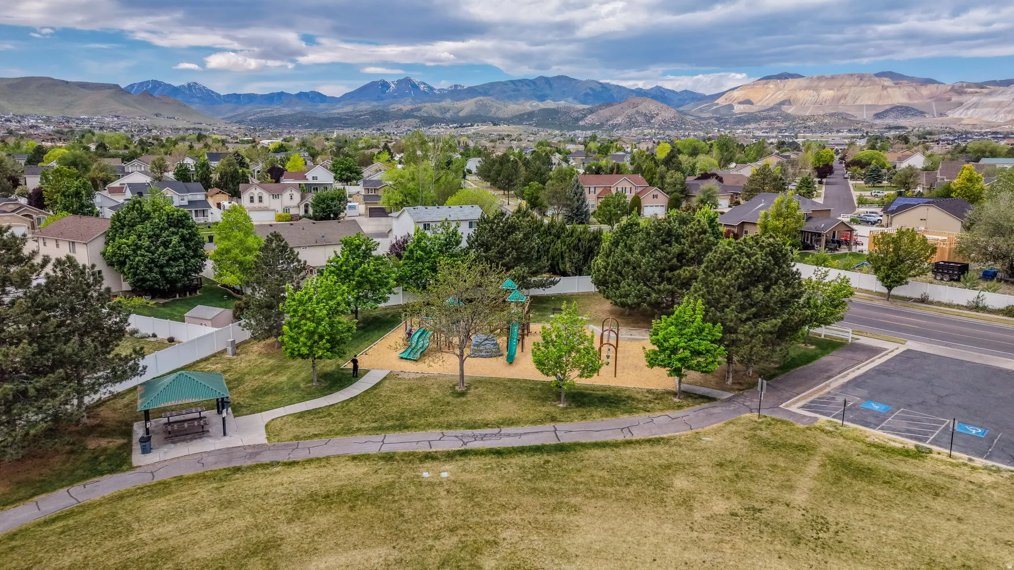 Community park featuring a green canopy, playground structure, covered picnic area, and paved pathways