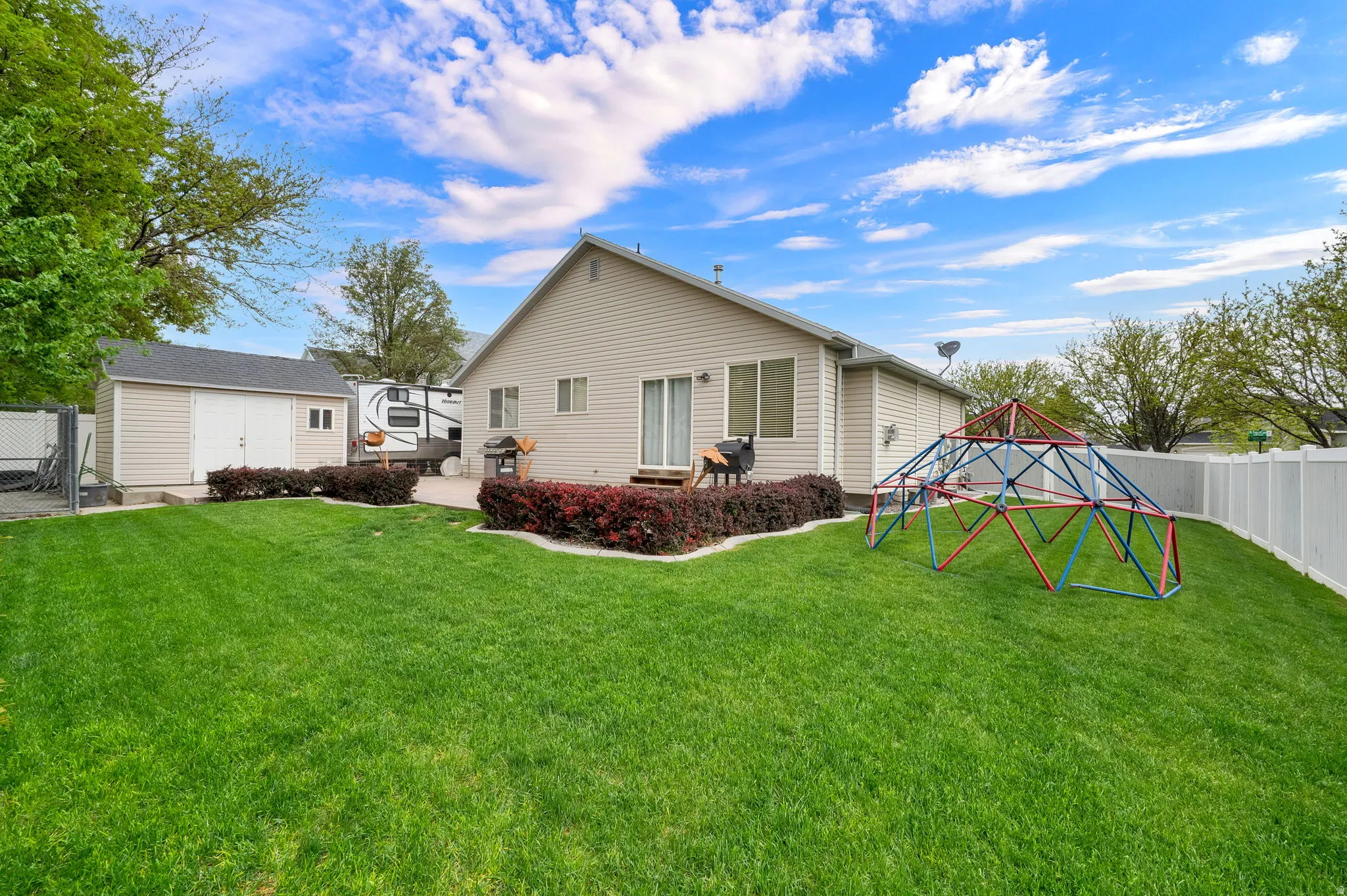 Expansive backyard featuring a manicured lawn, a concrete patio, and mature landscaping