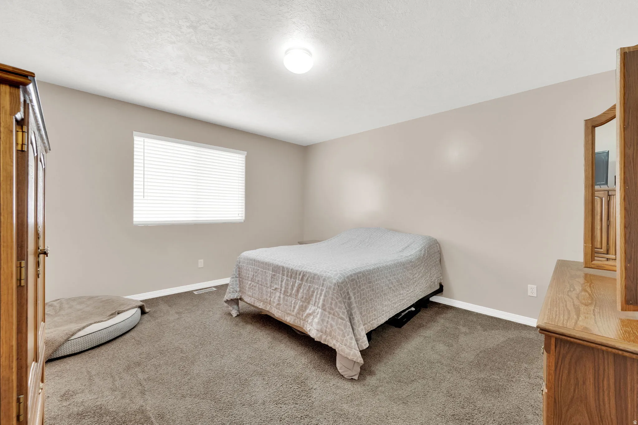 Carpeted room featuring neutral wall tones, a single window with blinds, and a ceiling-mounted light fixture