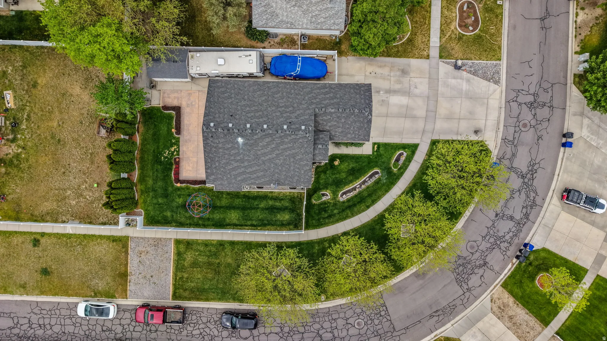 Overhead view of a residential property featuring a dark shingle roof, concrete driveway, and front lawn with mature trees