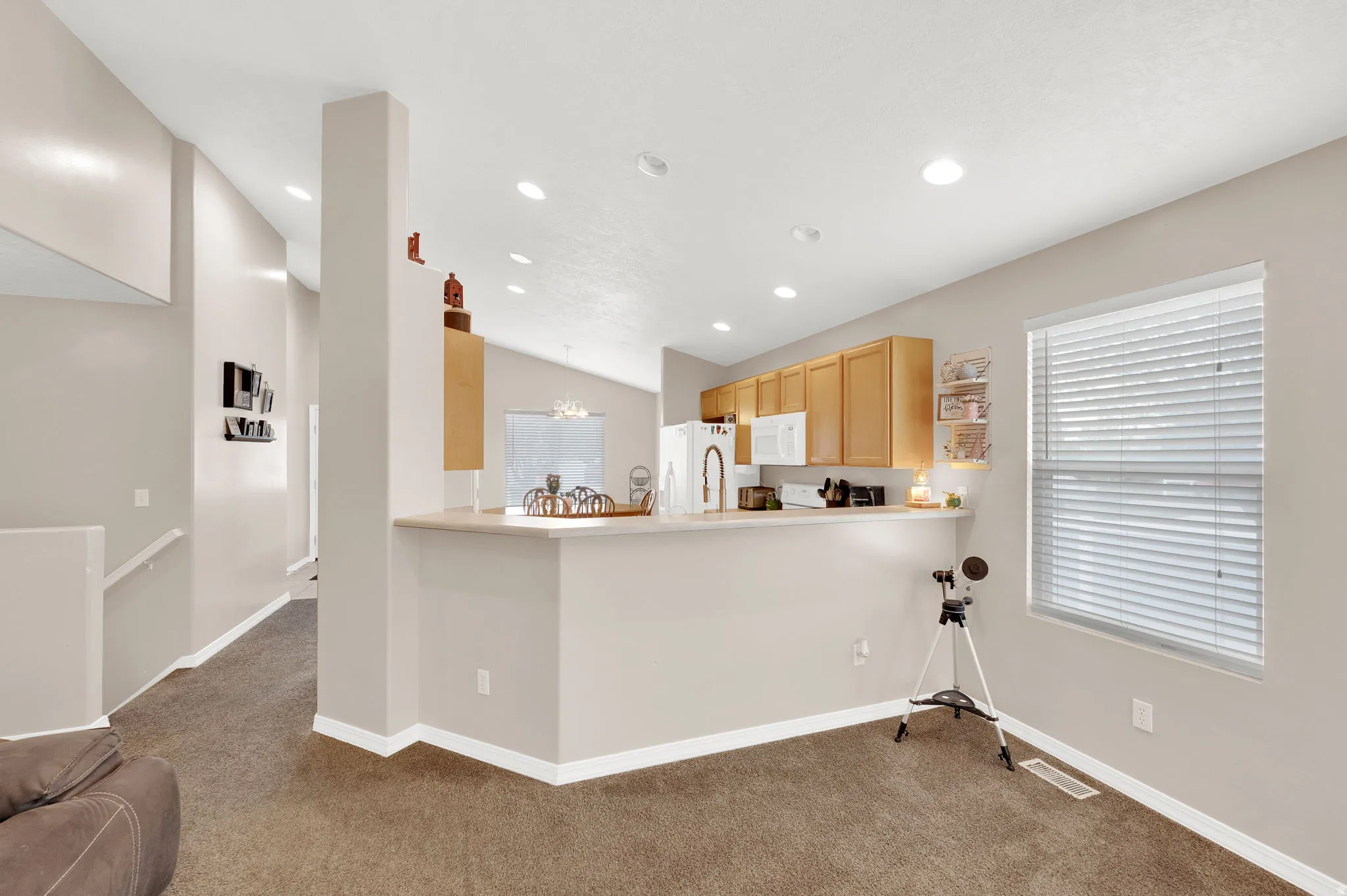 Open-concept living space featuring a kitchen with light wood cabinetry, white appliances, and a breakfast bar