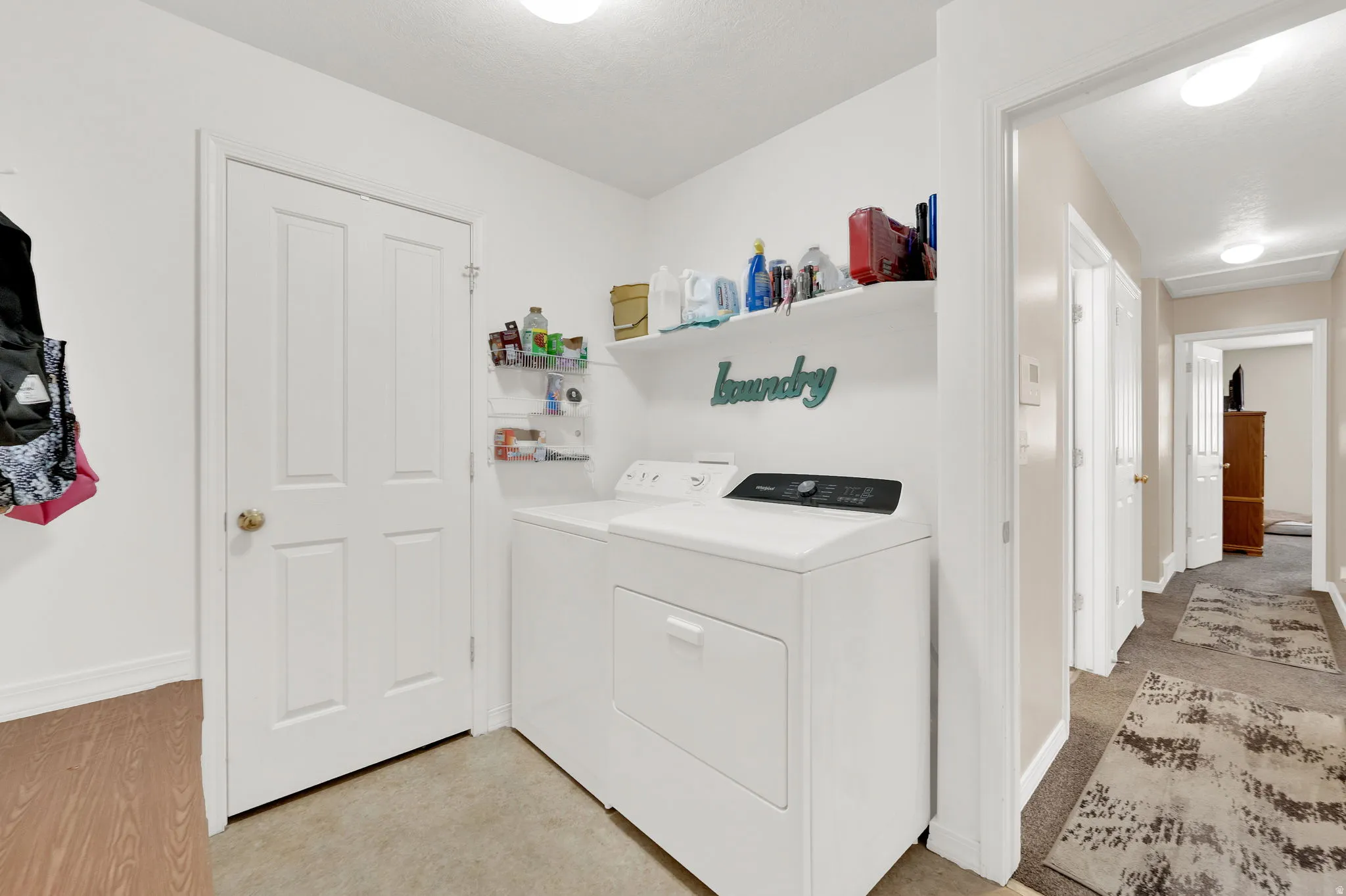 Dedicated laundry area featuring a full-size washer and dryer, an overhead shelving unit, and a durable flooring surface