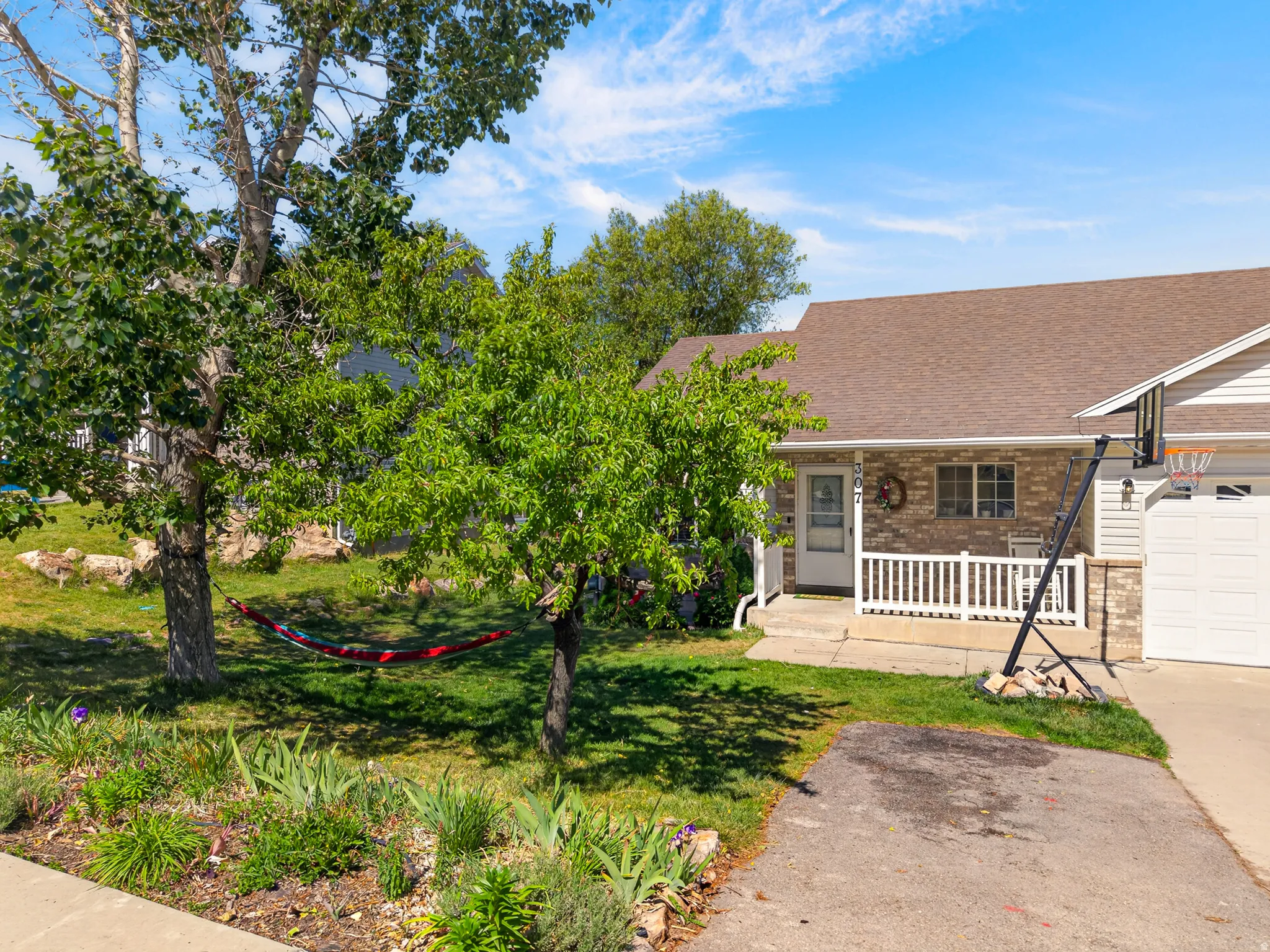 Brick facade home featuring a covered front porch with white railing, attached garage with white door, and a brown shingle roof