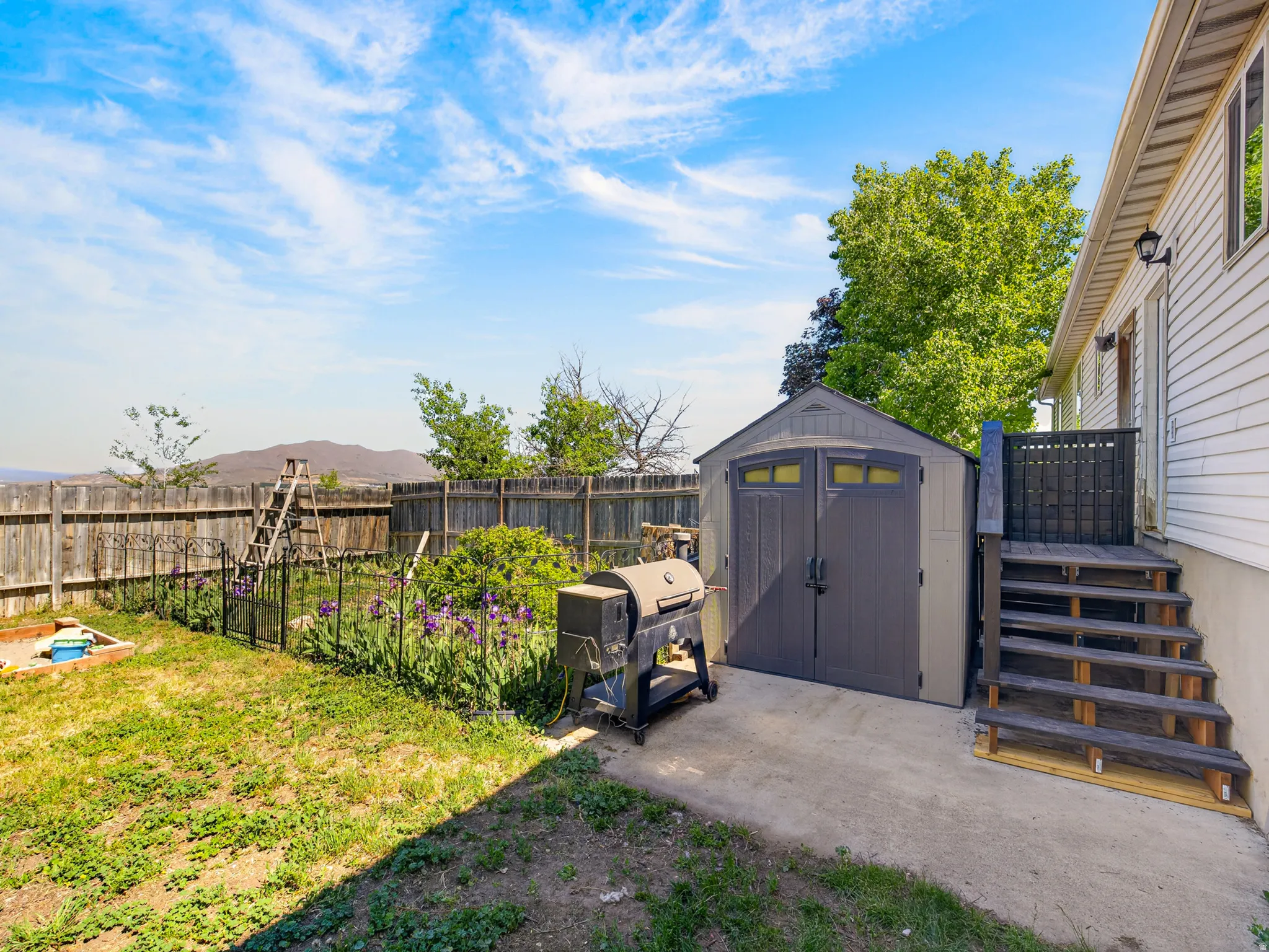Expansive backyard featuring a privacy fence, concrete patio, exterior stairs, and a storage shed