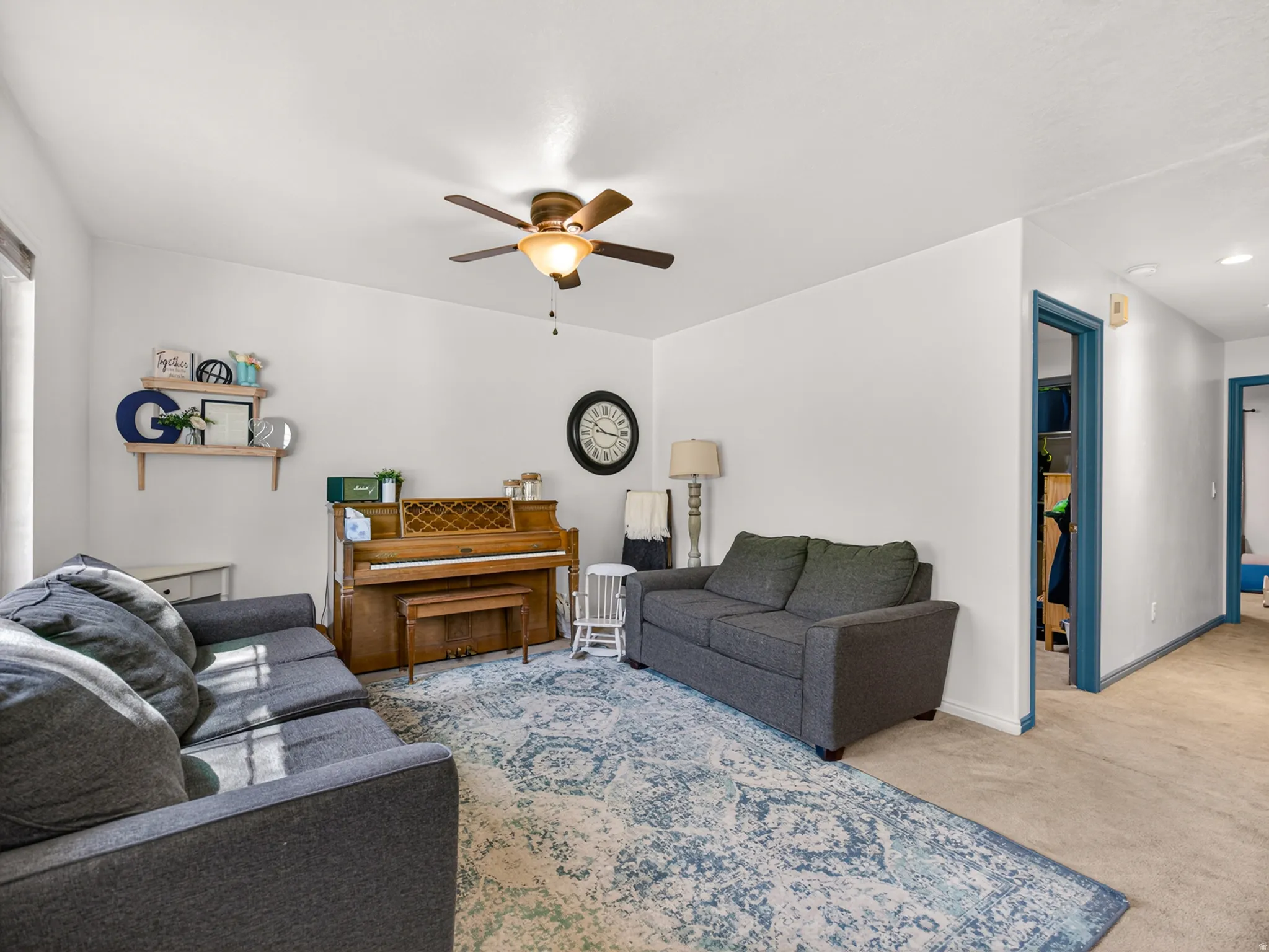 Living area featuring a ceiling fan with integrated lighting, light-colored walls, and carpeting