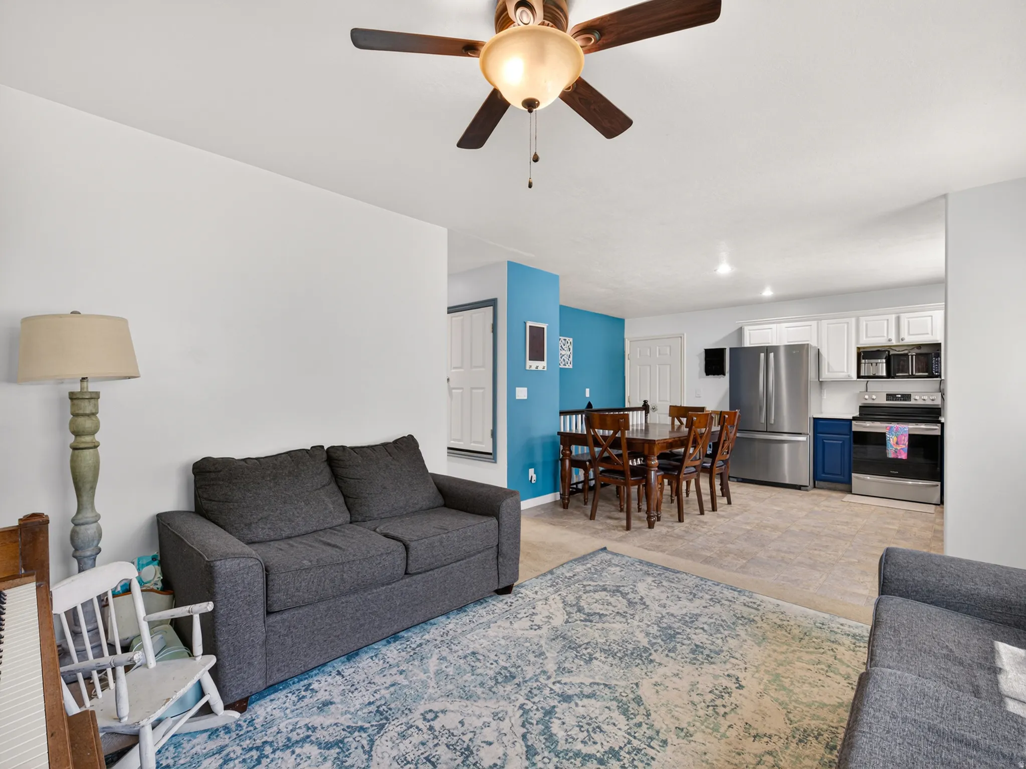 Integrated living and dining space featuring a ceiling fan, light-toned flooring, white walls, and a vibrant blue accent wall