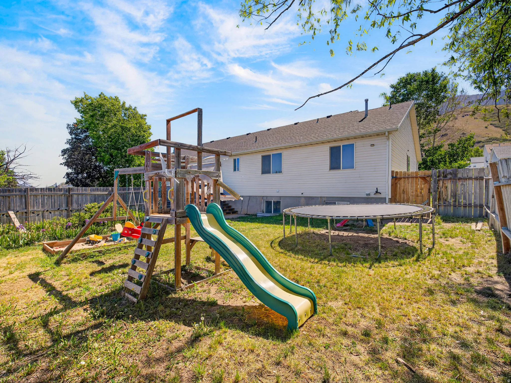 Spacious backyard featuring a light colored vinyl-sided exterior, a pitched shingle roof, a wood fence boundary, and a visible hillside backdrop