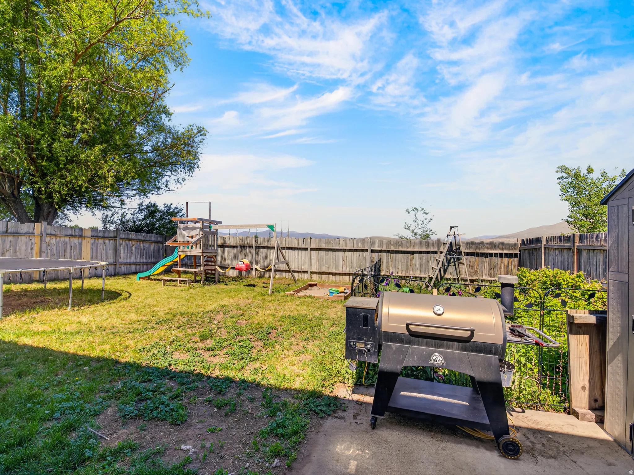 Expansive backyard featuring a mature tree, wood fencing, and a concrete patio area