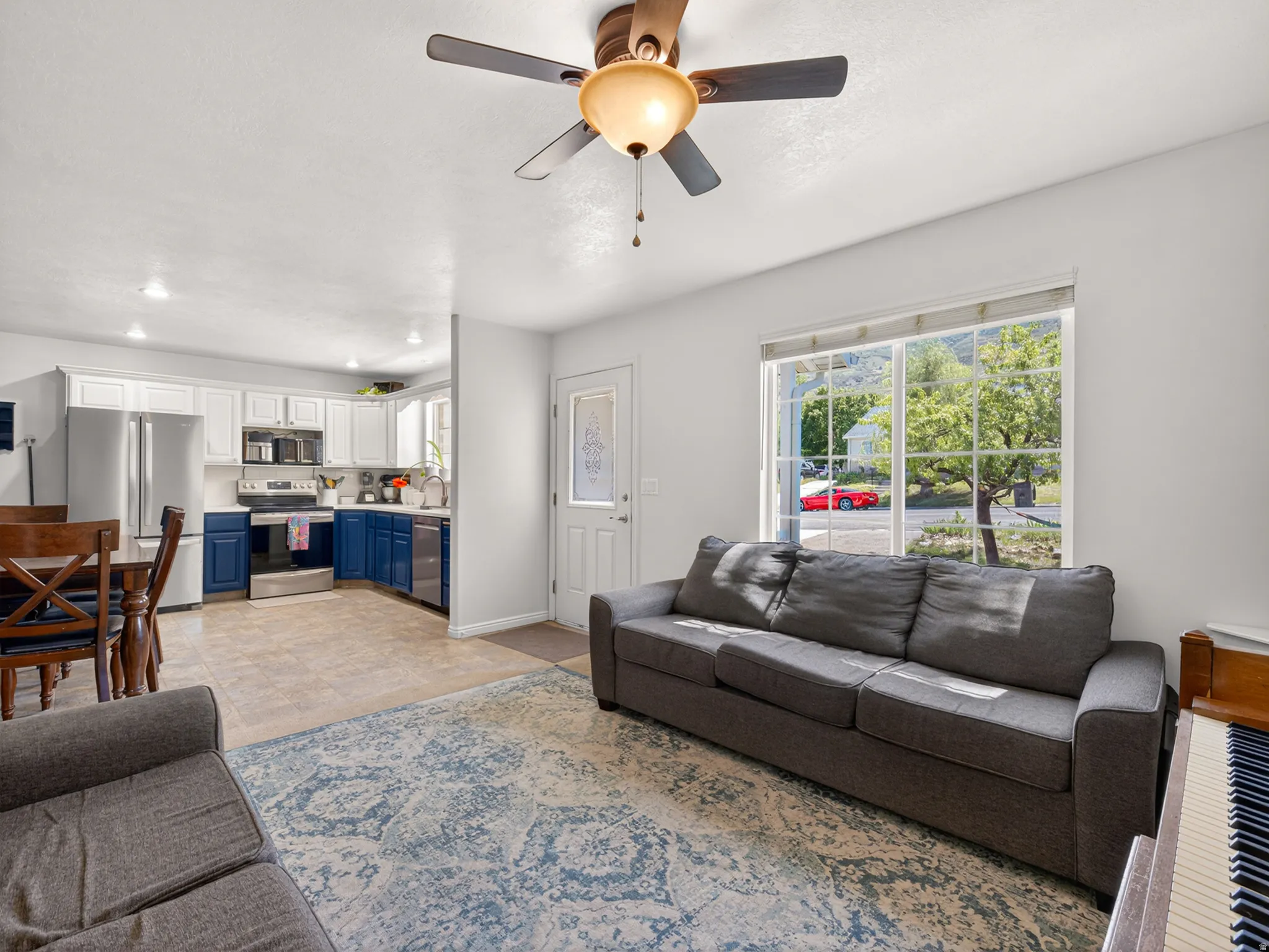 Open-concept living space featuring a ceiling fan with integrated lighting, a large window with white framing, and a front entry door with decorative glass