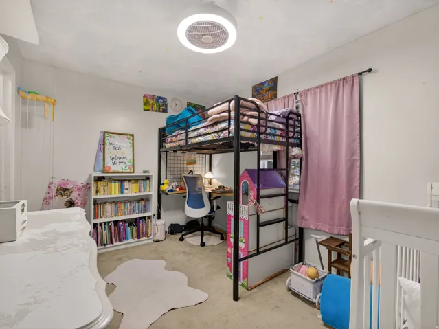 Secondary main floor bedroom featuring a loft bed structure with integrated desk space, a built-in white bookshelf, and a ceiling-mounted light fixture with fan