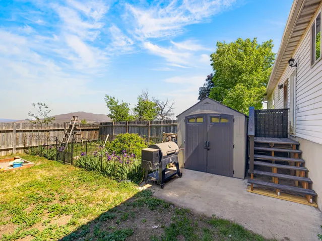 Expansive backyard featuring a privacy fence, concrete patio, exterior stairs, and a storage shed