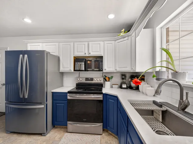Kitchen featuring white upper cabinetry, blue lower cabinetry, stainless steel appliances, white countertops, and a white subway tile backsplash