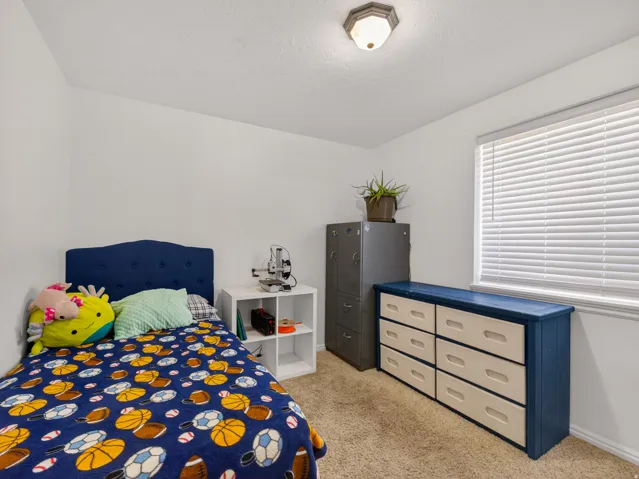 Secondary basement bedroom with ceiling mounted fixture, white walls, and a window with blinds