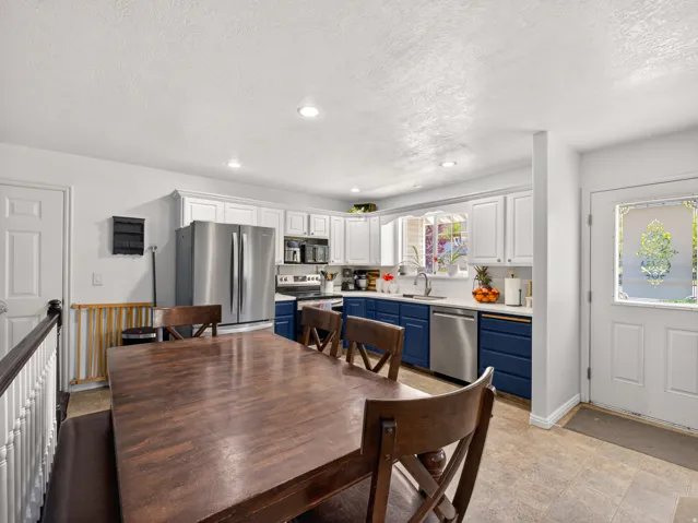 Bright kitchen featuring white upper cabinetry, contrasting blue lower cabinetry, stainless steel appliances, and a window above the sink