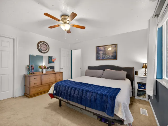 Primary bedroom featuring a ceiling fan with integrated lighting, multiple windows with white trim, and a paneled interior door