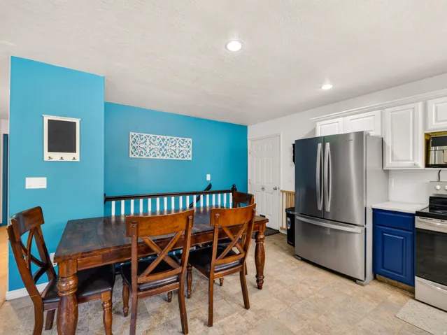 Kitchen area featuring white upper cabinetry, blue lower cabinetry, stainless steel appliances, and a linoleum floor