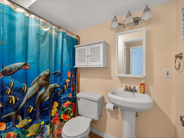 Basement bathroom with pedestal sink and chrome fixtures, framed mirror, and a three-light vanity bar