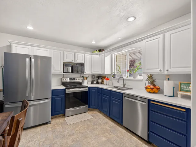 Kitchen featuring white upper cabinetry, navy blue lower cabinetry, stainless steel appliances, light-toned countertops, and a window above the sink