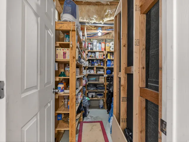 Basement storage area featuring extensive wood shelving, unfinished walls with visible framing and insulation, and a concrete floor
