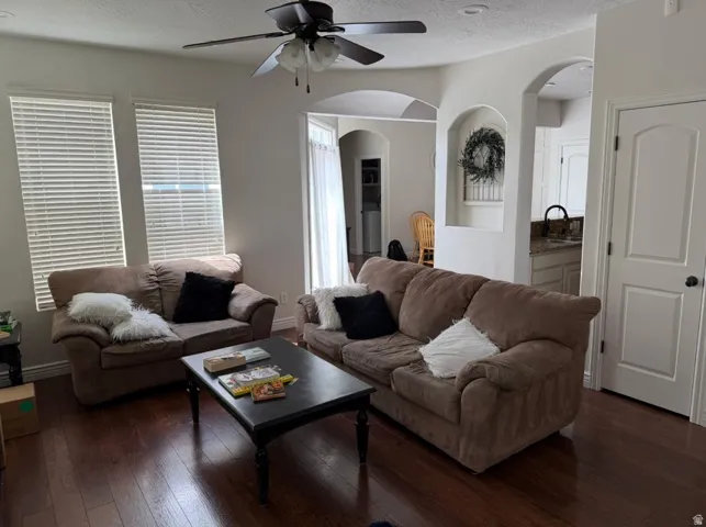 Spacious living area featuring wood-finish flooring, a ceiling fan, and multiple windows with blinds