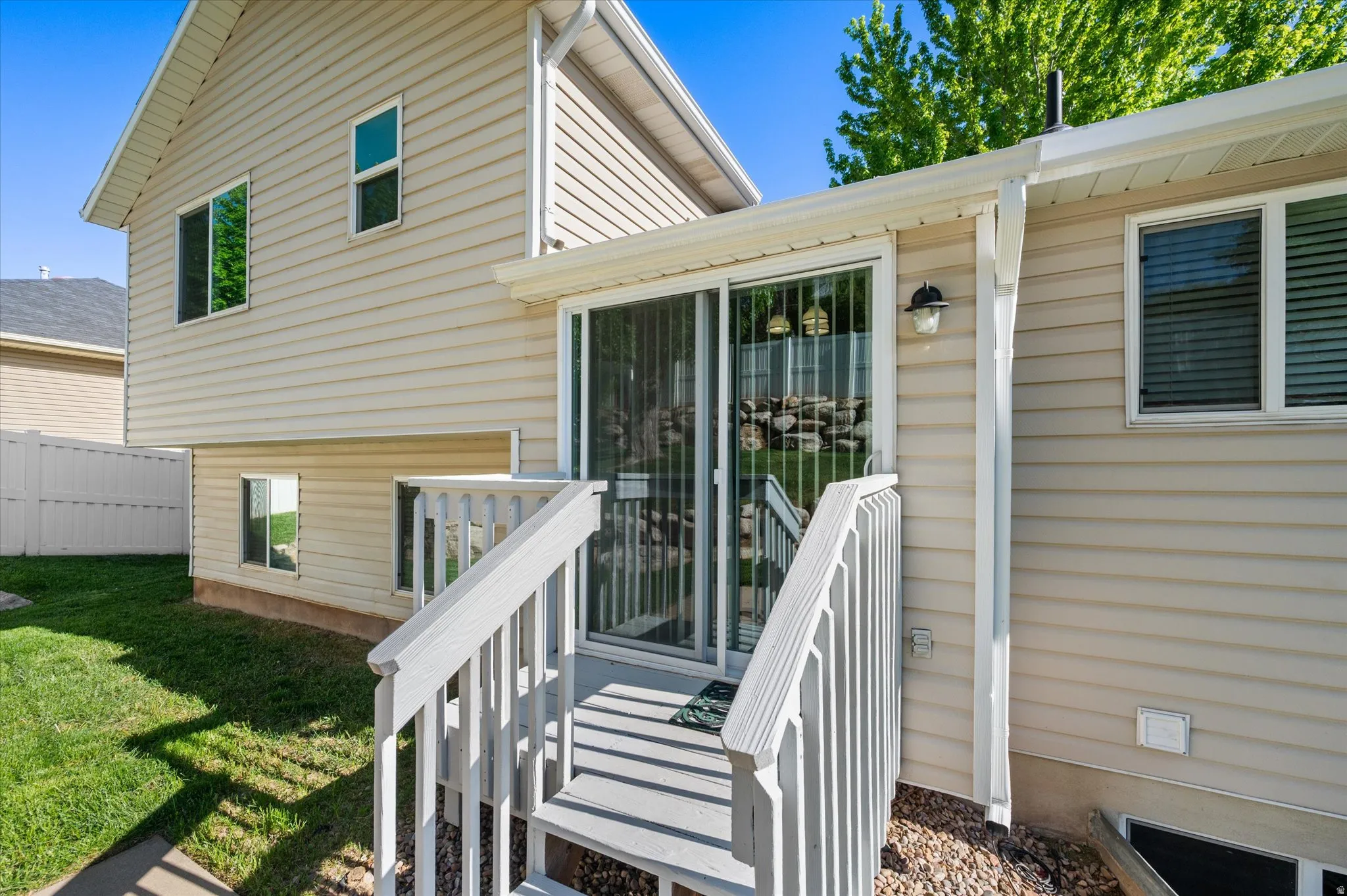 Rear exterior featuring light-colored siding, a sliding glass door, and a wooden staircase with railing