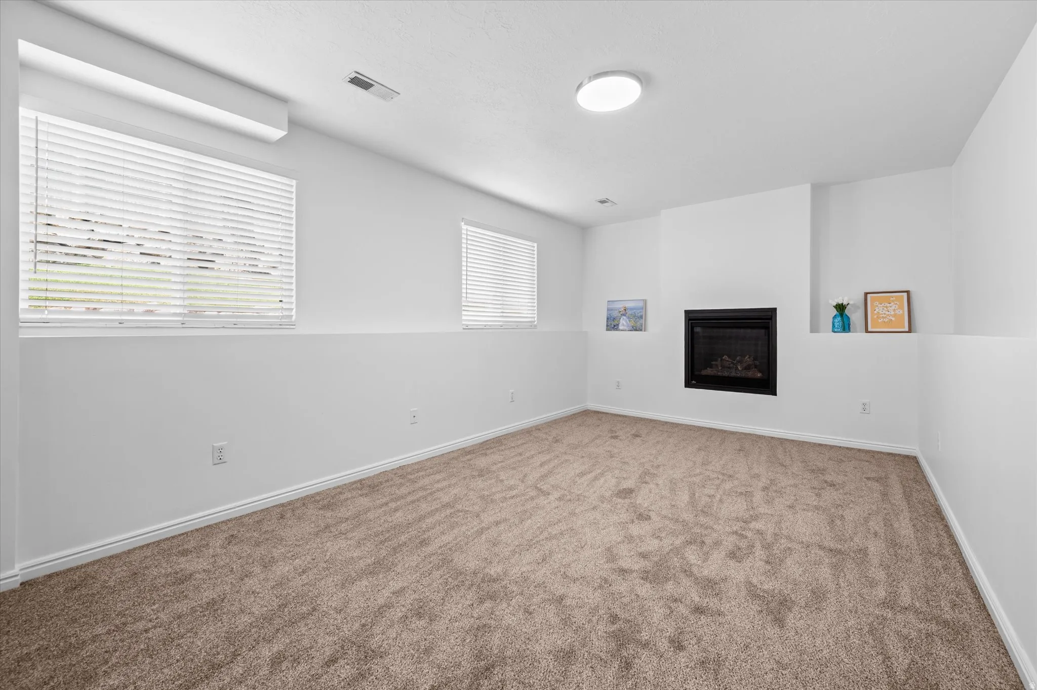 Room featuring a built-in fireplace with a black insert, light brown carpet, white walls, and two windows with blinds