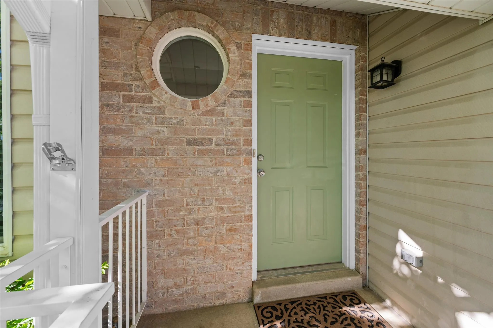 Entryway featuring a panel door, brick facade, circular window, and exterior wall sconce