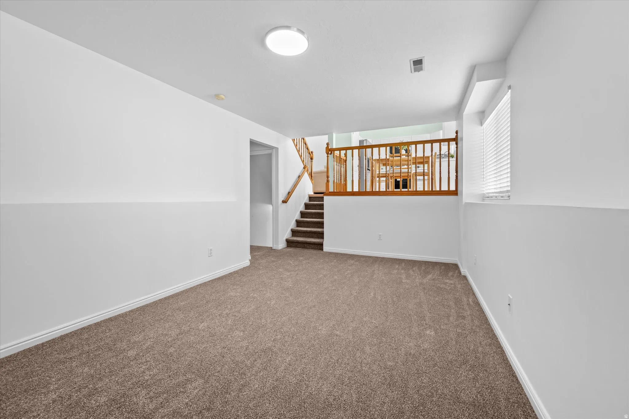 Spacious lower-level room featuring brown carpeting, white walls, and white baseboards