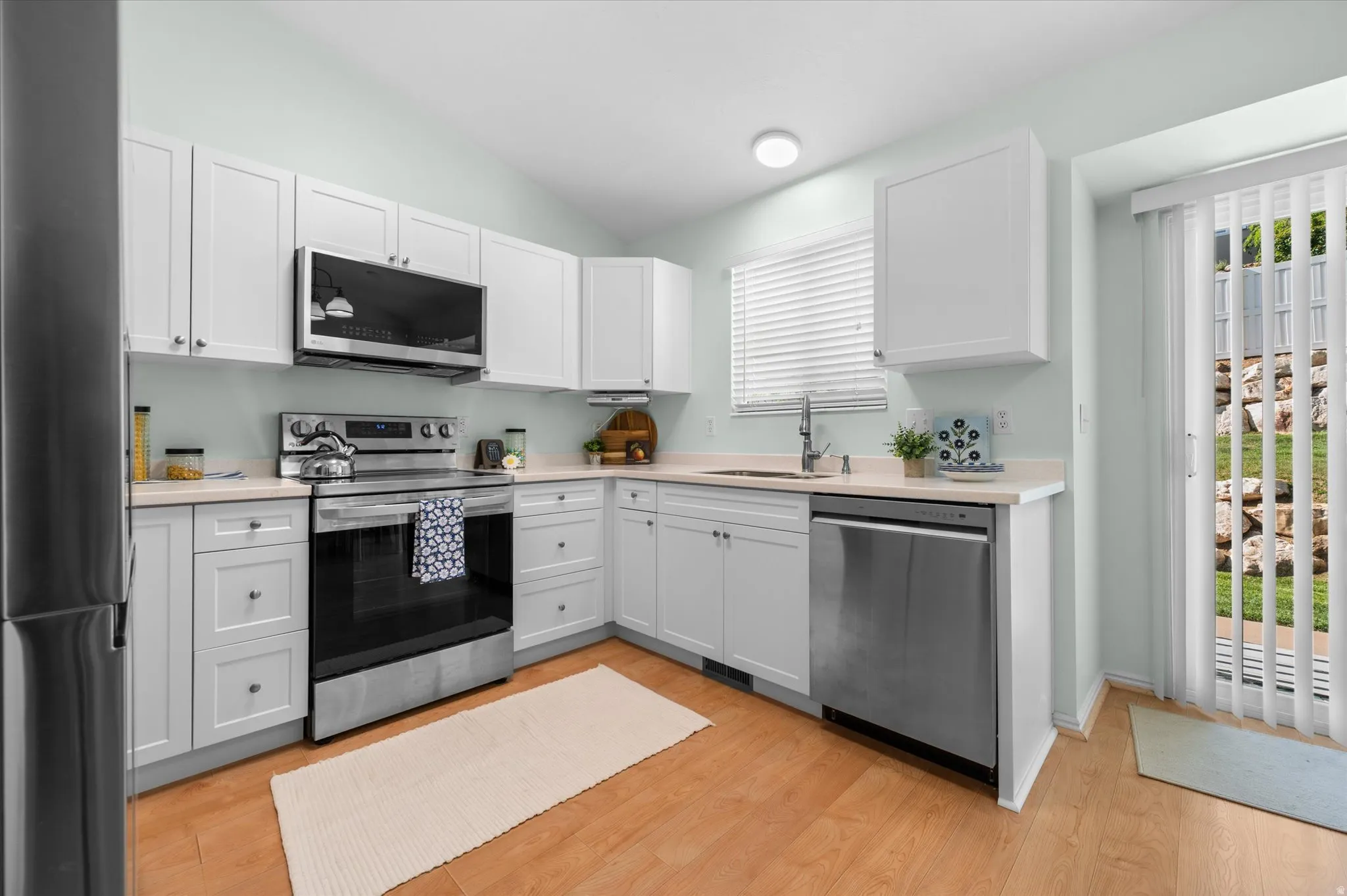 Kitchen featuring white cabinetry, light-toned countertops, stainless steel appliances, and wood-finish flooring