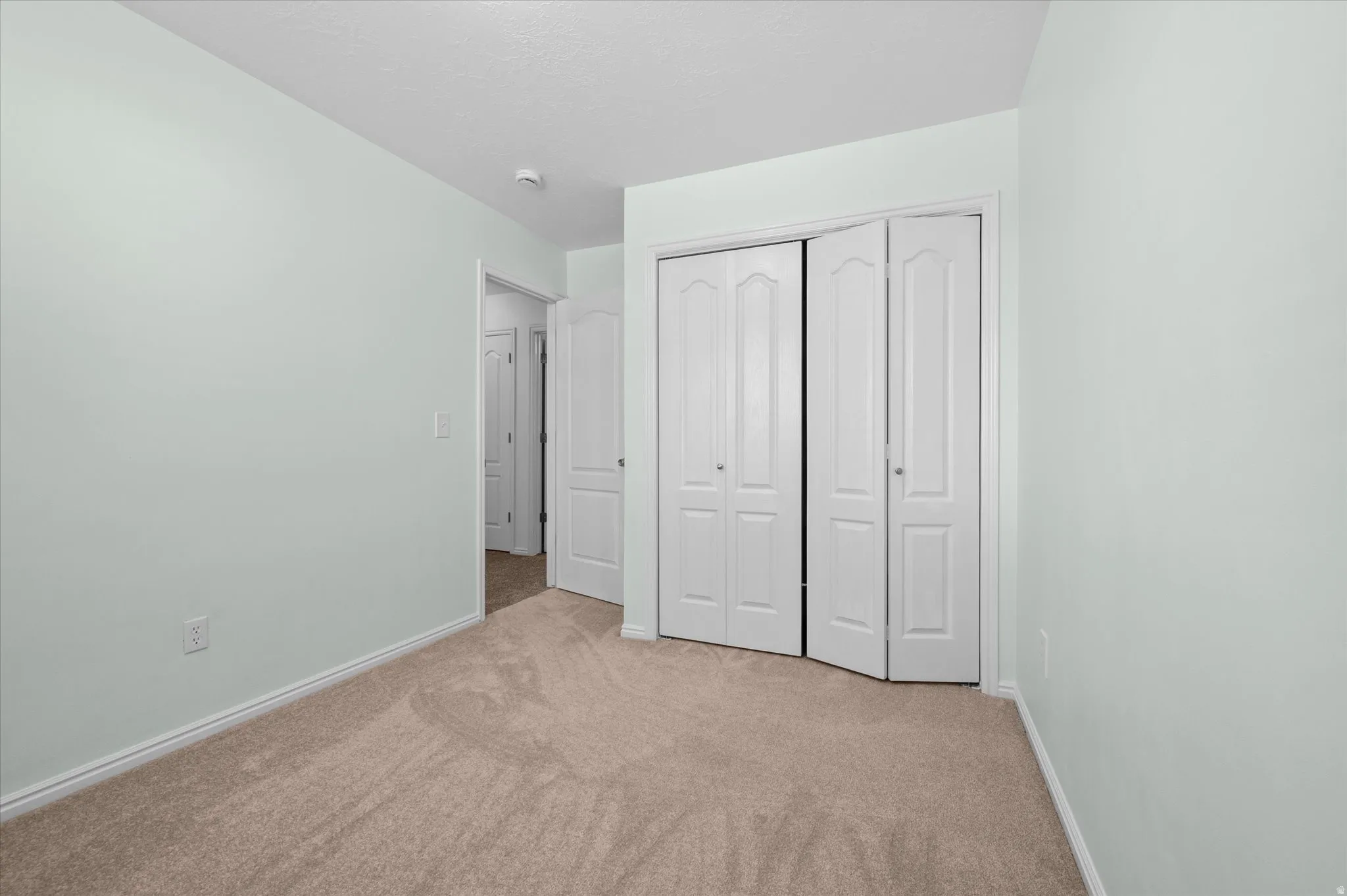 Carpeted room featuring light green walls, white baseboards, and bi-fold closet doors with panel detailing