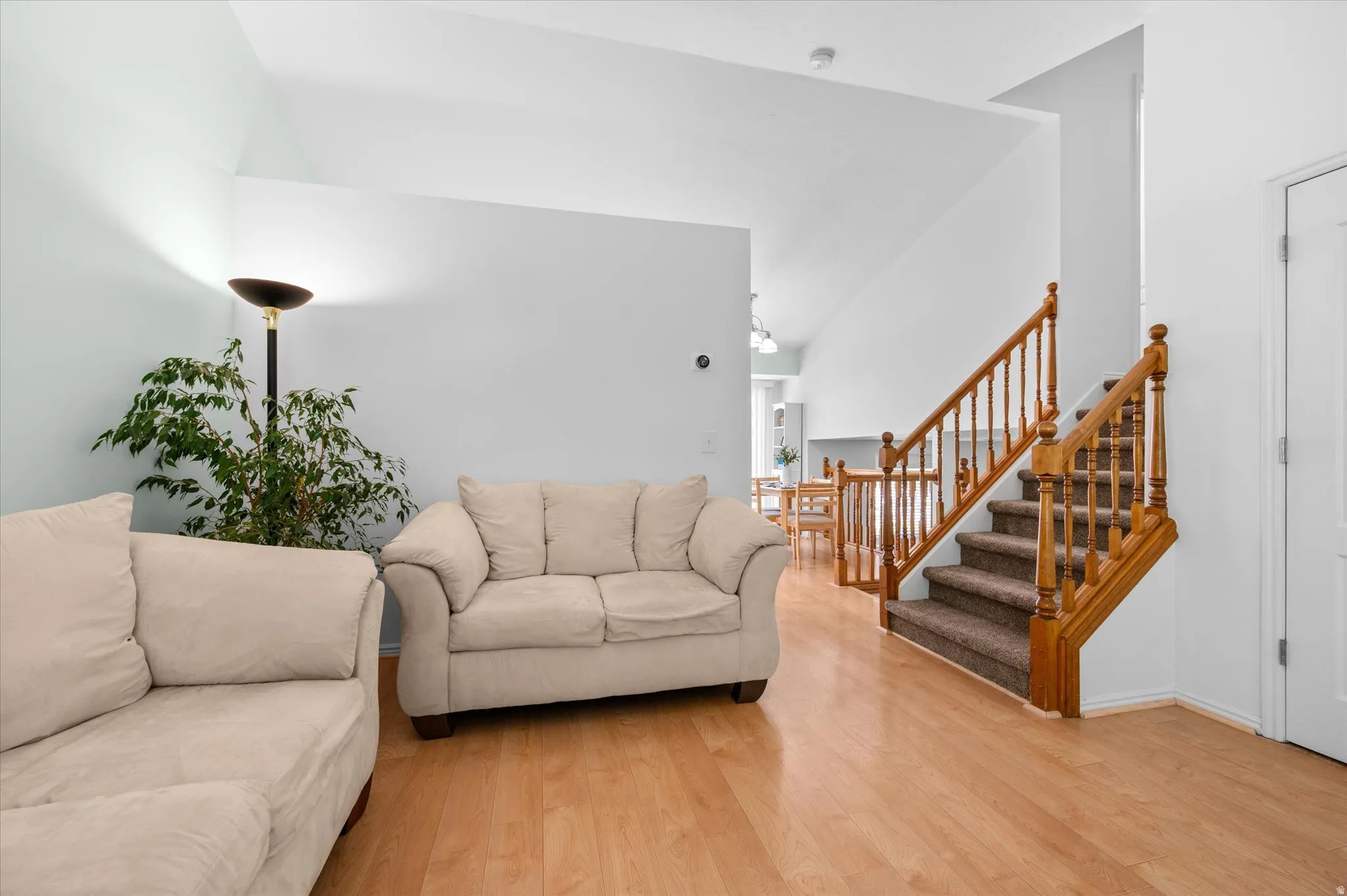 Open concept living space featuring vaulted ceilings, wood-finish flooring, and a staircase with wood banisters and carpeted treads
