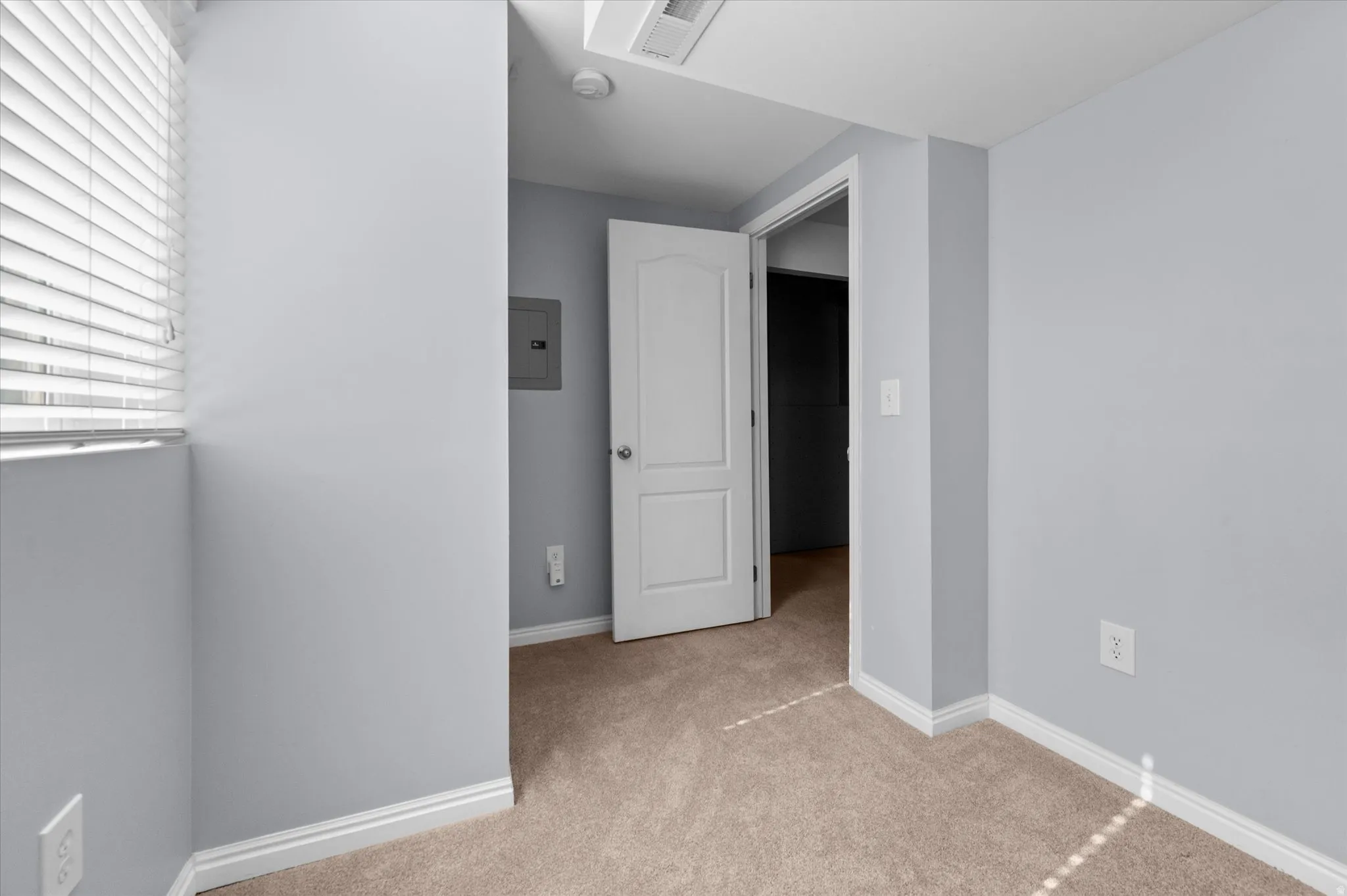 Carpeted room featuring light gray walls, white baseboards, and a window with horizontal blinds