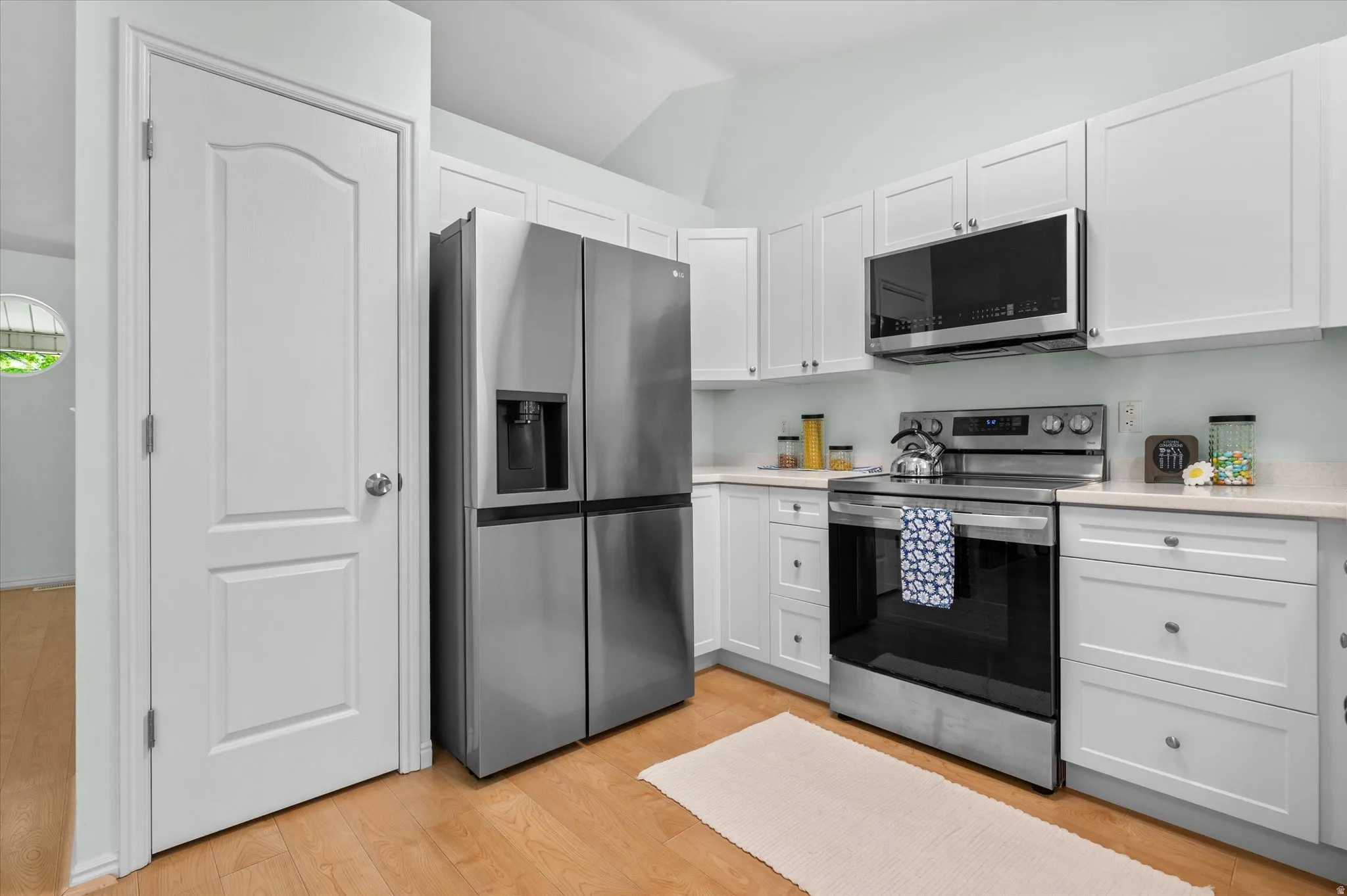 Contemporary kitchen featuring light wood-finish flooring and pristine white cabinetry