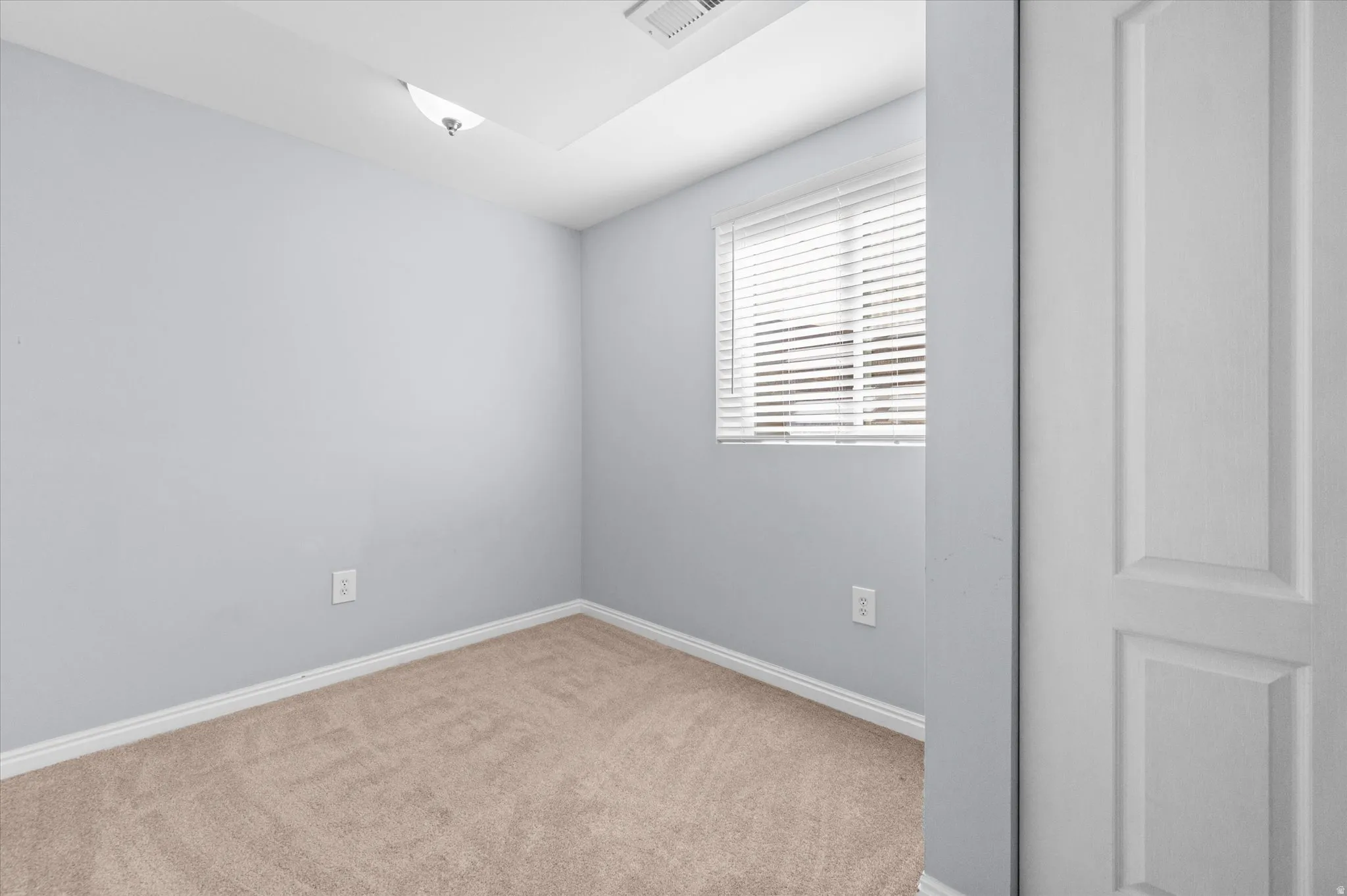 Neutral toned room featuring light gray walls, plush carpeting, and a window with blinds