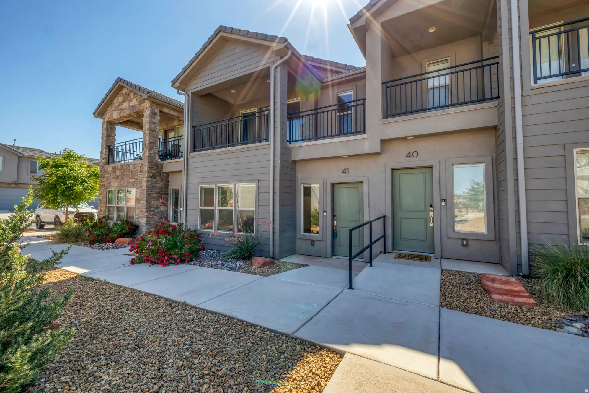 Contemporary facade featuring stone accents, multiple balconies with black railings, and a gravel and concrete entryway