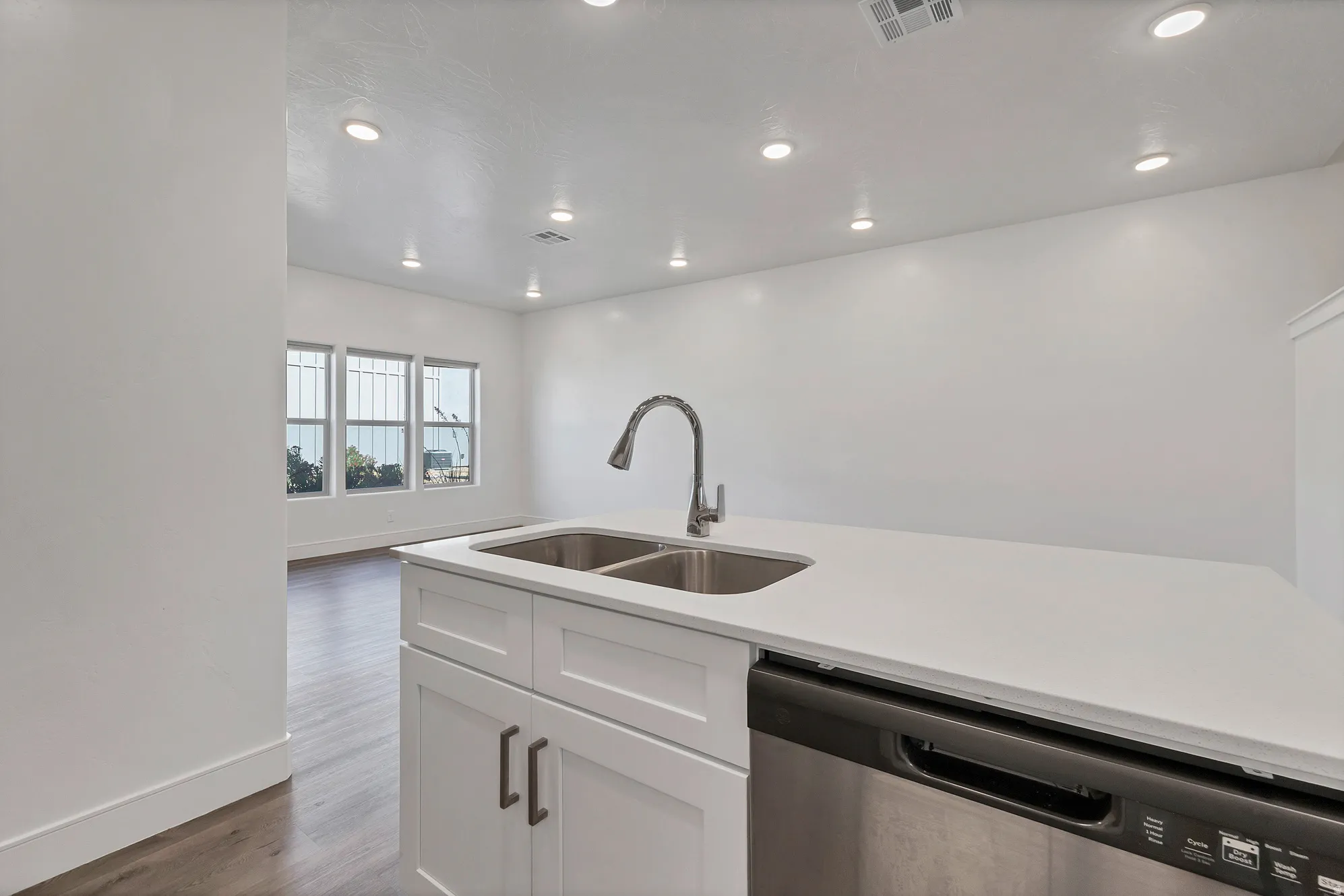 Kitchen island featuring a dual basin stainless steel sink with a gooseneck faucet, white cabinetry, and a built-in dishwasher